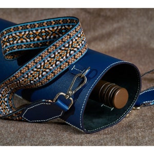 May include: A blue leather carrying case with a patterned strap. The case is designed to hold a bottle, which is partially visible inside.