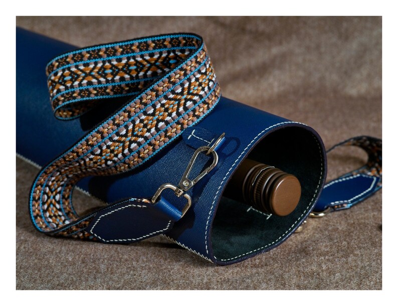 May include: A blue leather carrying case with a patterned strap. The case is designed to hold a bottle, which is partially visible inside.