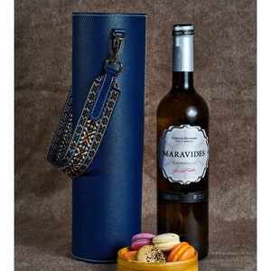 May include: A blue leather wine bottle carrier with a brown and blue patterned strap, a bottle of white wine labeled "Maravides Chardonnay", and a small bowl of colorful macarons.