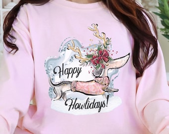 Peut inclure: Un sweat-shirt rose clair avec un motif de teckel festif. Le dessin représente un teckel portant un pull rose et des bois de renne, avec l'inscription "Happy Howlidays!". Le sweat-shirt a des manches longues.