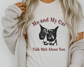 May include: A white t-shirt with a black and white cat graphic and the text "Me and My Cat Talk Shit About You" in maroon.