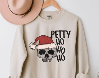 Könnte beinhalten: Beiges Sweatshirt mit einem Totenkopf, der einen Weihnachtsmannhut trägt. Der Text "Petty Ho Ho Ho" ist in Schwarz gedruckt. Ein hellbrauner Hut hängt über dem Sweatshirt.