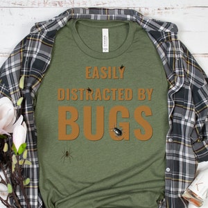 May include: A green t-shirt with the text "Easily Distracted By Bugs" in brown letters. The shirt has a variety of bug illustrations printed on it.
