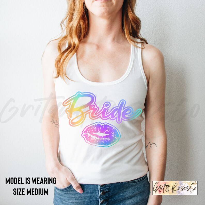 Puede incluir: Camiseta blanca de tirantes con el texto "Bride" en degradado arco&iacute;ris y una impresi&oacute;n de labios en degradado arco&iacute;ris.