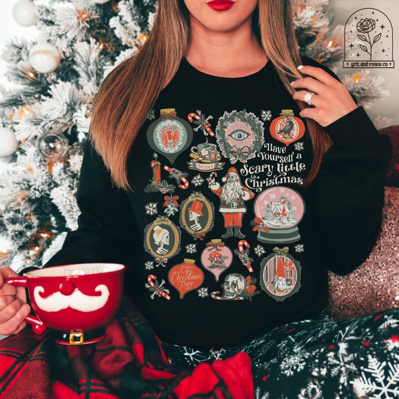 May include: Black sweatshirt with a festive Christmas design featuring a variety of spooky and whimsical illustrations. The text reads "Have Yourself a Scary Little Christmas".