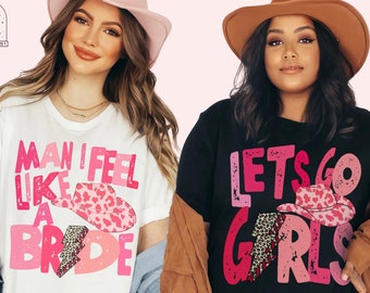 Puede incluir: Dos mujeres con camisetas gráficas. Una camiseta es blanca con el texto "MAN I FEEL LIKE A BRIDE" y un sombrero de vaquero rosa. La otra camiseta es negra con el texto "LETS GO GIRLS" y un sombrero de vaquero rosa.