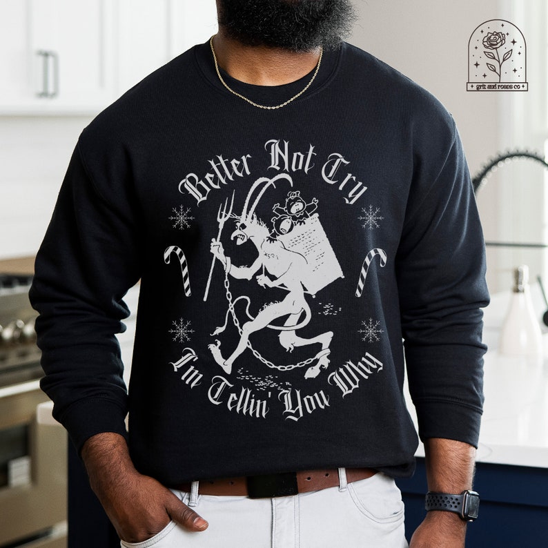 May include: Black sweatshirt with a white graphic of a devil carrying a sack, candy canes, and snowflakes. The text reads "Better Not Try, I'm Tellin' You Why". The sweatshirt has a crew neck.