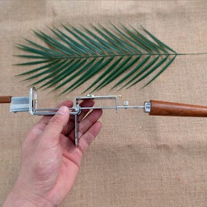 Op de afbeelding: Een kaassnijder met een roestvrijstalen frame en houten handvatten. De snijder heeft een draadmes en is ontworpen voor het snijden van kaas. De houten handvatten hebben een warme bruine kleur.