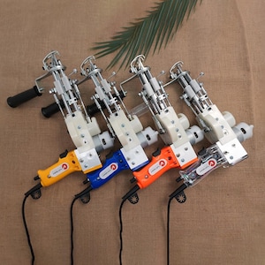 May include: A collection of rug tufting guns with colorful handles in yellow, blue, orange, and clear. The guns have a white body and black handles, with a black power cord. The tools are arranged on a brown surface.