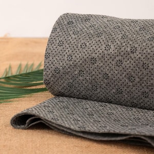May include: Rolled gray non-slip rug with a textured surface. The rug is partially unrolled, revealing the underside with a pattern of small, dark dots. The rug is made of a soft, flexible material.