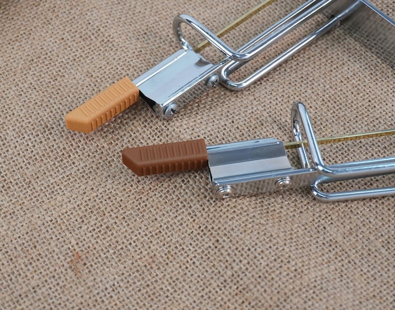 Op de afbeelding: Twee metalen klemmen met bruine en bruin rubberen handgrepen. De klemmen hebben een zilveren afwerking en een gebogen handvat. De rubberen handgrepen zijn rechthoekig met een geribbelde textuur. De achtergrond is een bruin, getextureerd weefsel.