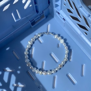 May include: A white pearl bracelet with a silver clasp, resting on a blue plastic crate.