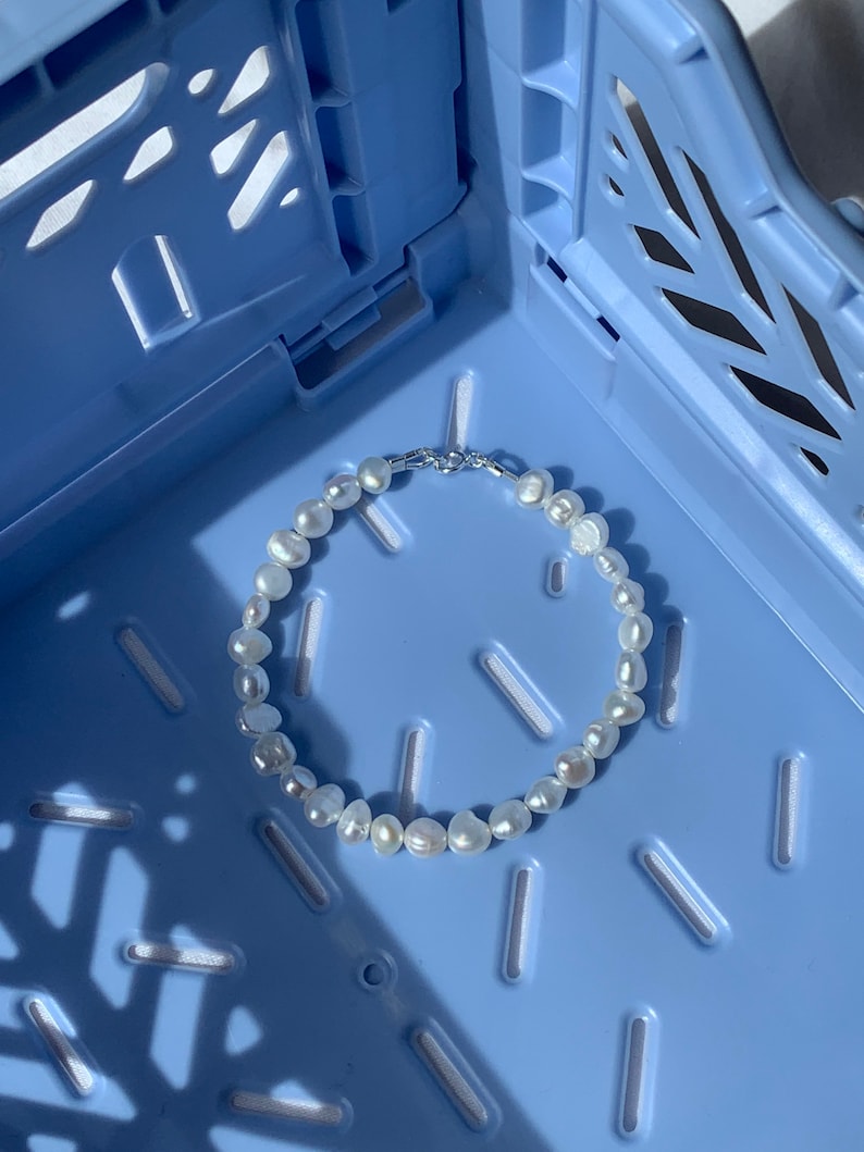 May include: A white pearl bracelet with a silver clasp, resting on a blue plastic crate.