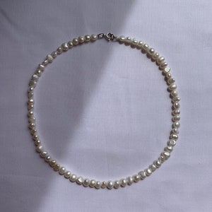 May include: A white pearl necklace with a silver clasp. The pearls are irregular in shape and size, giving the necklace a unique and natural look.