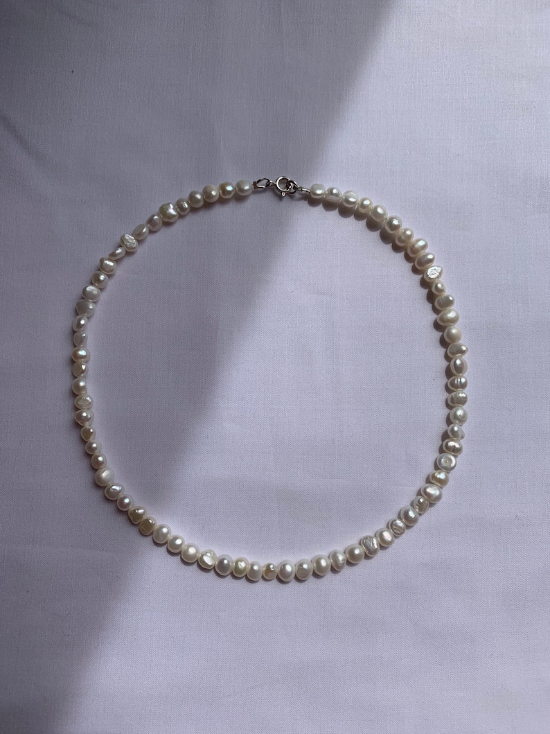May include: A white pearl necklace with a silver clasp. The pearls are irregular in shape and size, giving the necklace a unique and natural look.