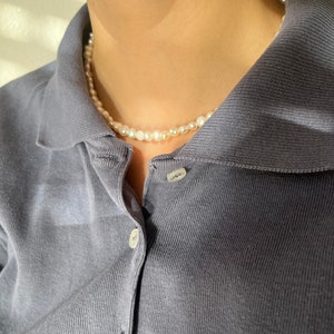 May include: A simple pearl necklace on a person wearing a dark blue collared shirt.