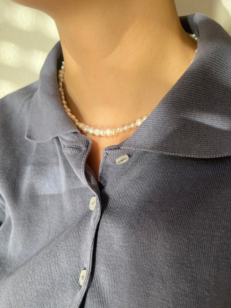 May include: A simple pearl necklace on a person wearing a dark blue collared shirt.
