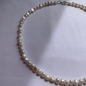 May include: A white pearl necklace with a silver clasp. The pearls are irregular in shape and size.
