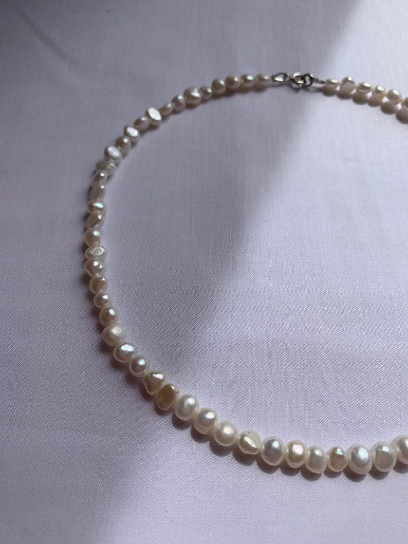 May include: A white pearl necklace with a silver clasp. The pearls are irregular in shape and size.
