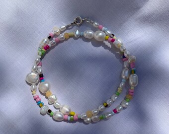 May include: A white pearl necklace with colorful beads. The necklace is made of small, round pearls and colorful beads in shades of pink, blue, green, yellow, and brown.