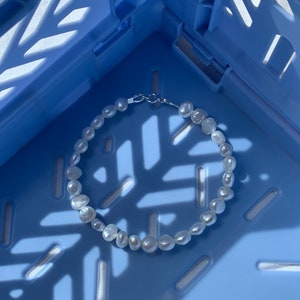 May include: A white pearl bracelet with a silver clasp, photographed on a blue plastic crate.