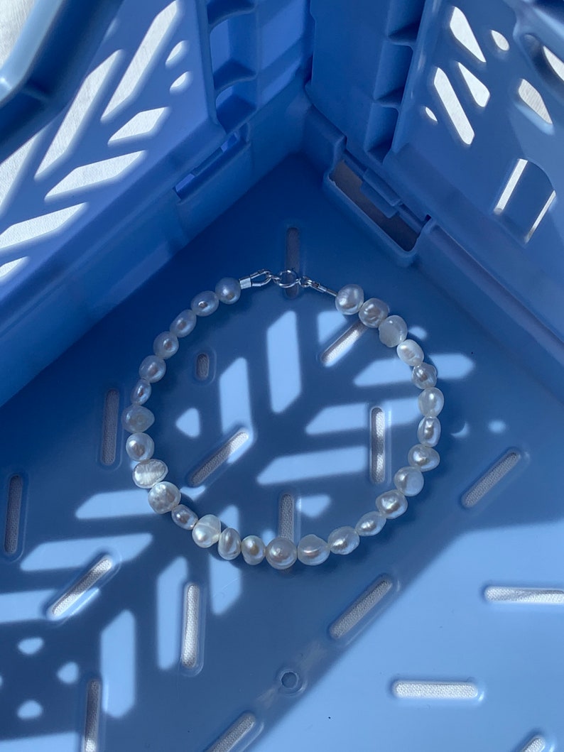 May include: A white pearl bracelet with a silver clasp, photographed on a blue plastic crate.