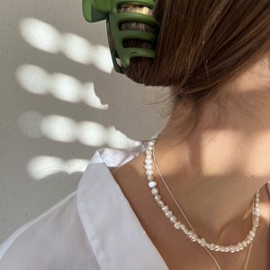 May include: A white pearl necklace with a silver heart pendant charm. The necklace is layered over a silver chain.