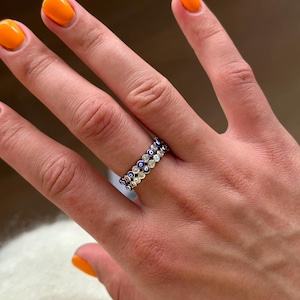 Könnte beinhalten: Ein silberner Ring mit einer doppelten Reihe von blauen und weißen bösen Augen-Anhängern. Der Ring wird an einem Finger getragen.