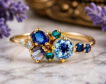 May include: A gold ring featuring a cluster of gemstones in shades of blue, teal, and white. The ring has a delicate band and a central arrangement of round and pear-shaped stones. The gemstones are set in a gold setting.