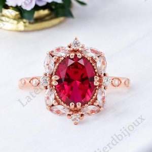 May include: A rose gold ring with a large oval ruby surrounded by smaller diamonds. The ring has a delicate, vintage-inspired design.