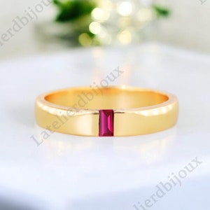 May include: A gold band ring with a single, rectangular, ruby red gemstone set in the centre.