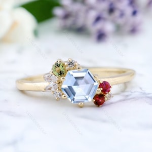 May include: A gold ring featuring a hexagonal blue topaz gemstone, surrounded by smaller green, red, and white gemstones.