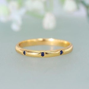 May include: A thin gold band ring with three small blue sapphires set into the band.