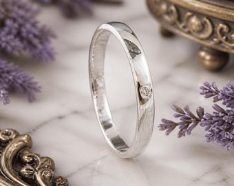 May include: A polished silver ring with a single, small diamond. The ring is set against a backdrop of purple lavender and a marble surface, with a decorative antique-style jewelry box in the background.