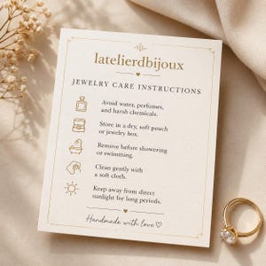 Puede incluir: Un anillo de oro con una piedra preciosa transparente junto a una tarjeta crema con instrucciones de cuidado de joyas. La tarjeta tiene el texto "latelierdbijoux" y "Handmade with love".