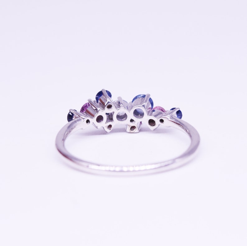 Puede incluir: Un anillo de plata con un grupo de piedras preciosas redondas en tonos azules y rosas. El anillo tiene una banda fina y pulida, y las piedras est&aacute;n engastadas juntas, creando un dise&ntilde;o floral o de estrella. El anillo est&aacute; sobre un fondo blanco.