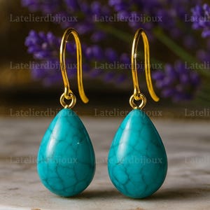 Puede incluir: Un par de pendientes colgantes dorados con piedras turquesas en forma de l&aacute;grima. Los pendientes tienen un dise&ntilde;o de gancho simple. El fondo est&aacute; borroso, con el texto "Latelierdbijoux".
