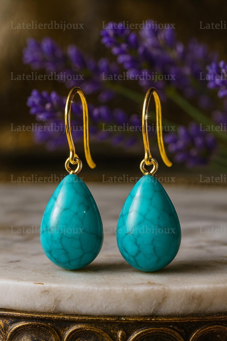 Puede incluir: Un par de pendientes colgantes dorados con piedras turquesas en forma de l&aacute;grima. Los pendientes tienen un dise&ntilde;o de gancho simple. El fondo est&aacute; borroso, con el texto "Latelierdbijoux".