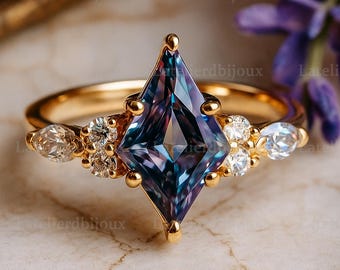 Puede incluir: Un anillo de oro con una gran piedra preciosa en forma de cometa, con tonos azules y morados. El anillo está adornado con piedras preciosas más pequeñas y transparentes, sobre un fondo de mármol.