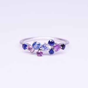 Puede incluir: Un anillo de plata con un grupo de gemas coloridas. El anillo presenta piedras redondas en tonos de azul, morado y rosa. Las gemas est&aacute;n engastadas juntas, creando un dise&ntilde;o brillante y llamativo.