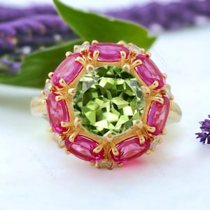 May include: A gold ring featuring a large green gemstone encircled by smaller pink gemstones and a few small clear gemstones.