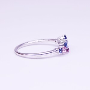 Puede incluir: Un anillo de plata con un grupo de piedras preciosas azules y rosas. El anillo tiene una banda delgada y pulida, y las piedras preciosas est&aacute;n dispuestas en un patr&oacute;n floral o abstracto. Las piedras preciosas son una mezcla de cortes redondos y marquesa.