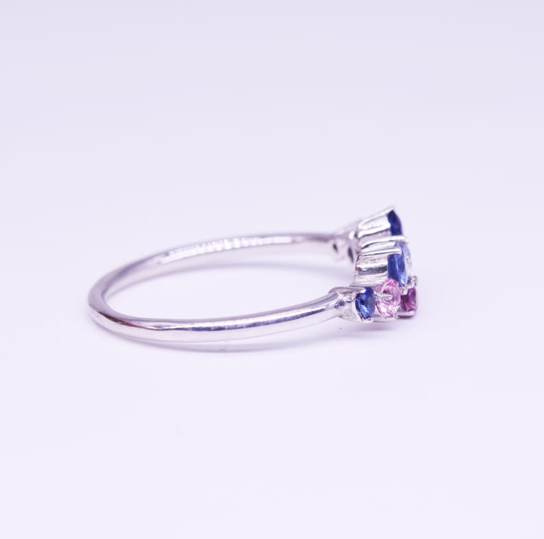 Puede incluir: Un anillo de plata con un grupo de piedras preciosas azules y rosas. El anillo tiene una banda delgada y pulida, y las piedras preciosas est&aacute;n dispuestas en un patr&oacute;n floral o abstracto. Las piedras preciosas son una mezcla de cortes redondos y marquesa.