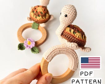 May include: Crochet turtle rattle toy with a wooden ring. The turtle is brown, orange, and yellow with a pink flower on the ring. The toy is handmade and comes with a PDF pattern.