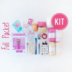 May include: A crochet kit for making a Barbie doll. The kit includes yarn in pink, white, and beige, a crochet hook, a pattern, and other supplies. The kit is labeled "Full Packet" and "KIT".