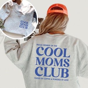 Könnte beinhalten: Grauer Pullover mit dem Text "PROUD MEMBER OF THE COOL MOMS CLUB FUELED BY COFFEE & POWERED BY LOVE" in blauer Schrift.