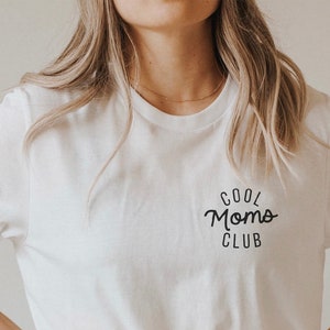 Könnte beinhalten: Weißes T-Shirt mit einem schwarzen Aufdruck, der in kursivschrift "Cool Moms Club" lautet.