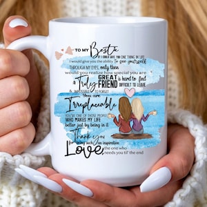 May include: White ceramic mug with a friendship theme. The mug features the text "To My Bestie" and a message about friendship, along with an illustration of three friends. The mug is held by a person.