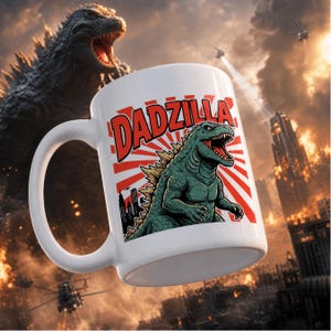 May include: A white ceramic mug featuring a graphic print of a green monster with the text DADZILLA in bold red letters. The design includes a red sunburst background and a silhouette of a city skyline, set against a dramatic scene of a giant monster.
