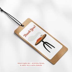 May include: A brown tag with a white rectangle featuring a cartoon table with a book and steam, and the words "Thank You!" in red. The tag is attached to a black string.
